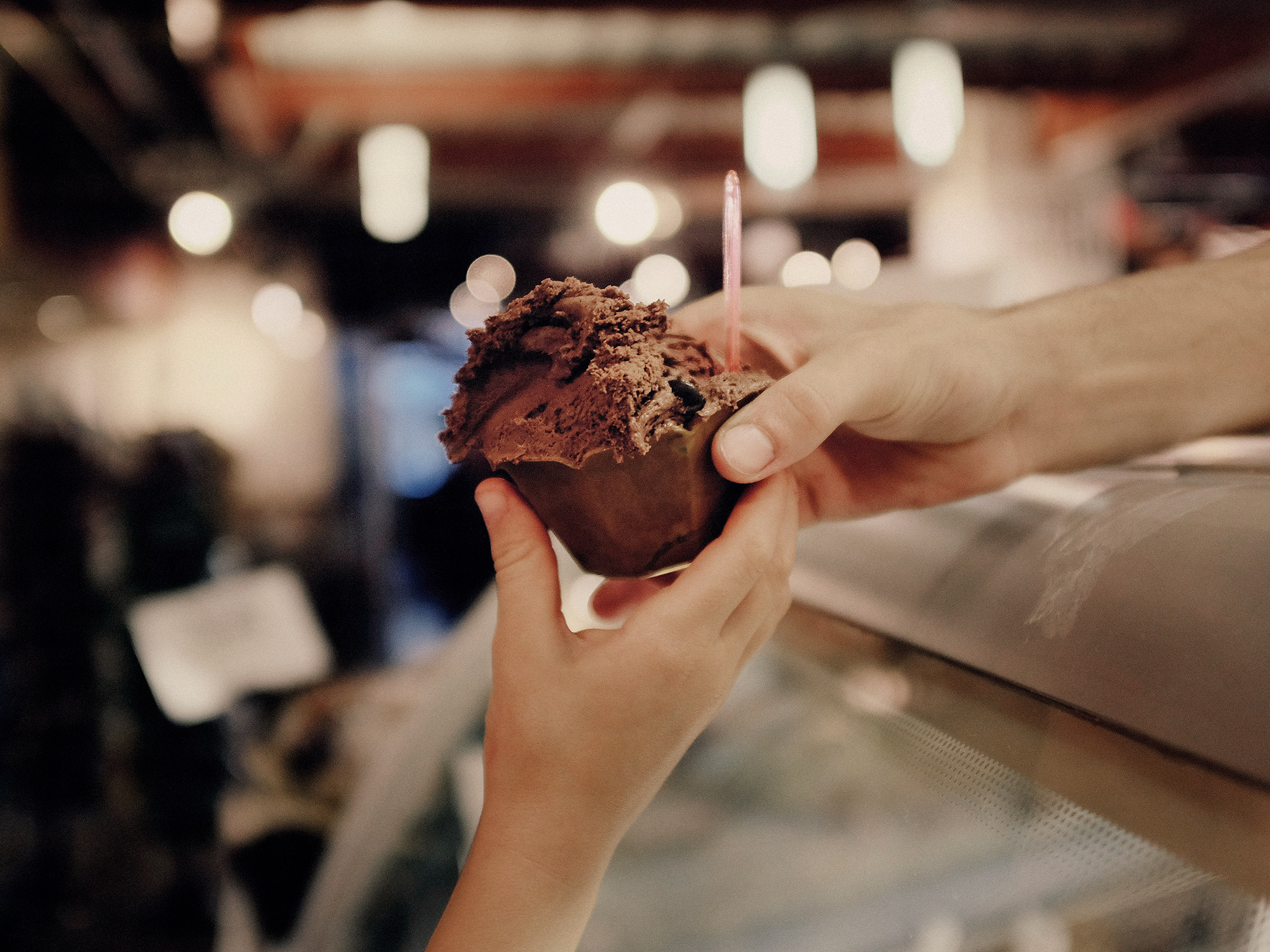 An ice cream parlor employee hands a child a scoop of ice cream, photographed by Todd Spoth, in The Woodlands, Texas.