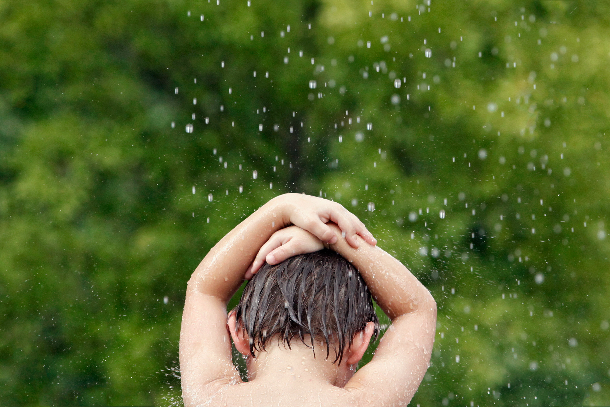 A boy plays in a water fountain at Discovery Green park in downtown Houston, Texas, photographed by Todd Spoth.