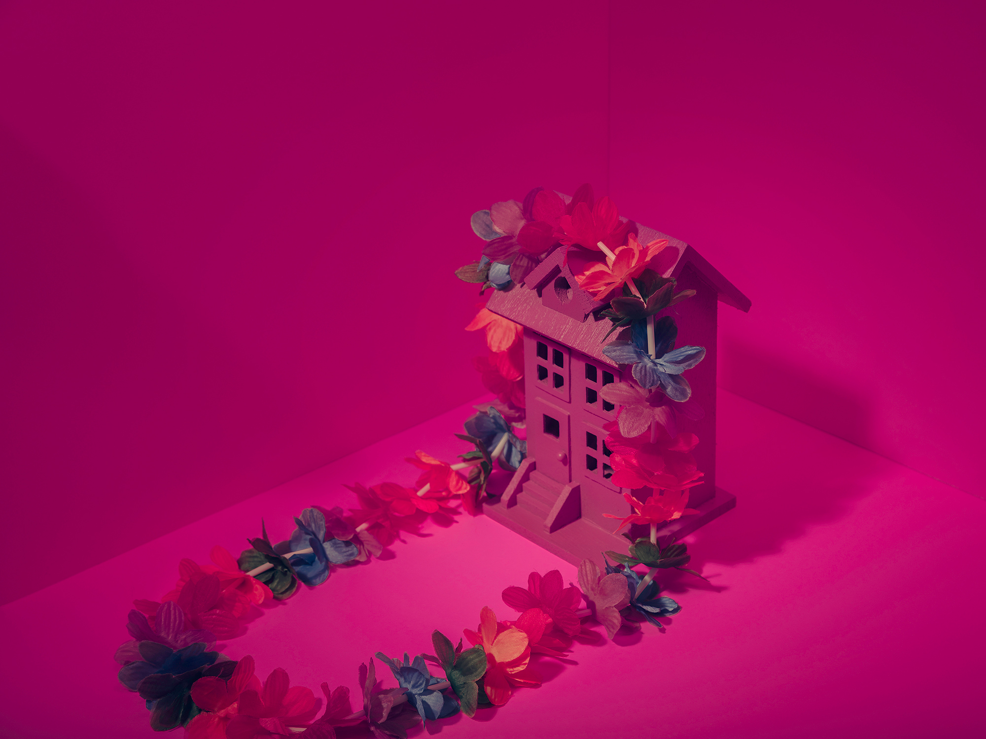 A pink model home with a Hawaiian lei draped over the top of it with a pink background, photographed in studio, by Houston photographer, Todd Spoth.